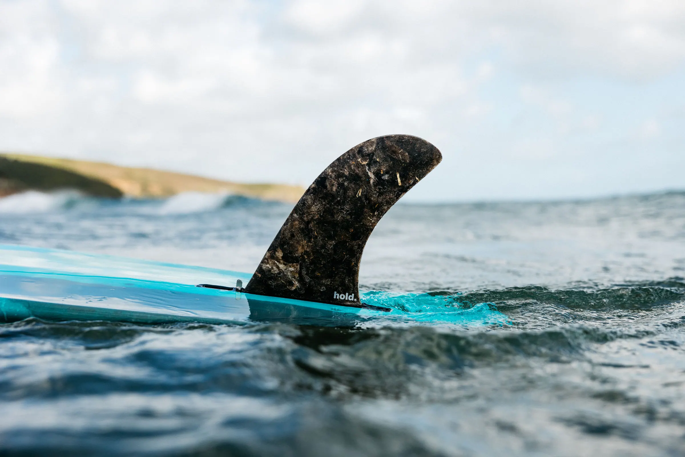A Hold fin cutting through coastal water on a turquoise surfboard.