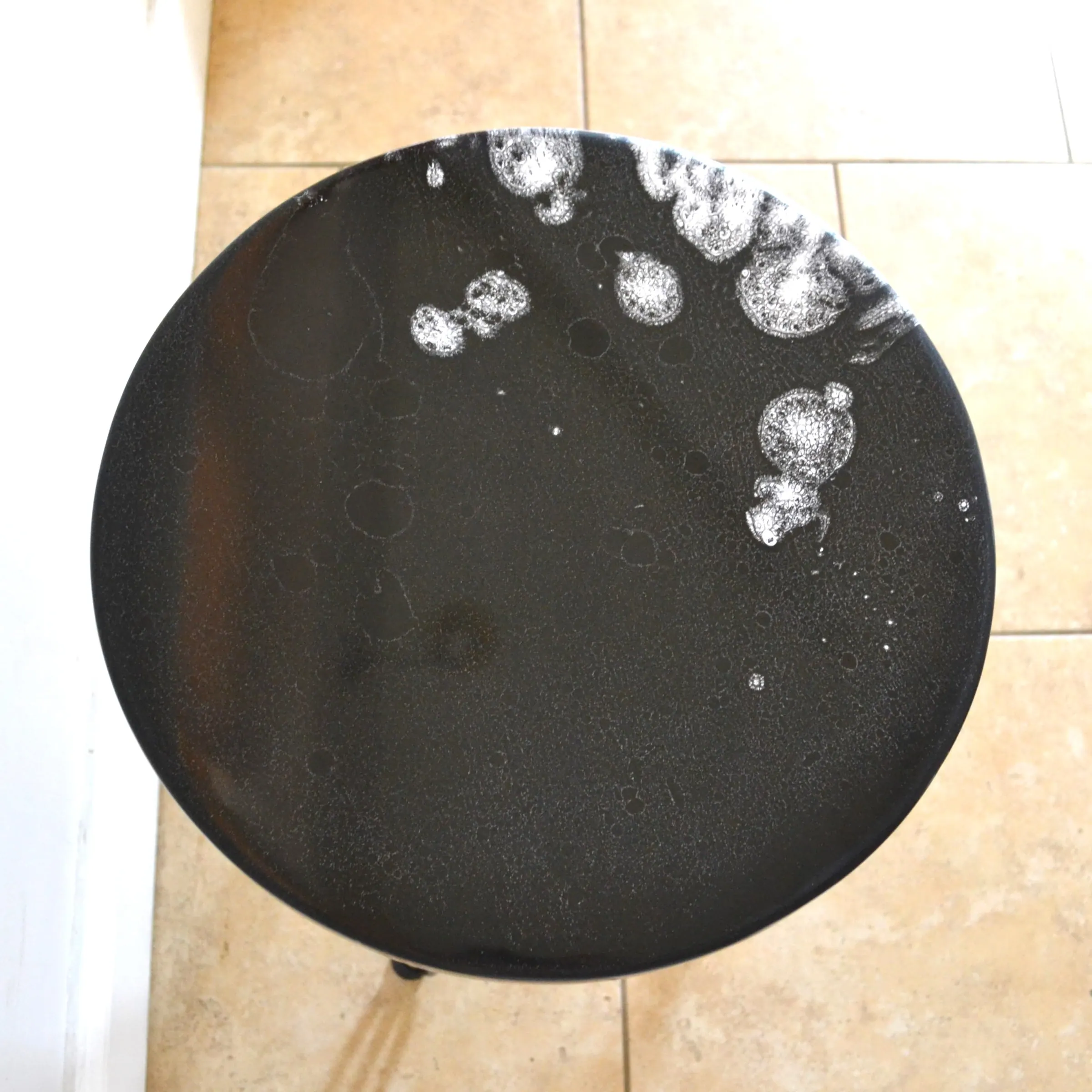 Overhead detail of a black round tabletop with white resin marks.