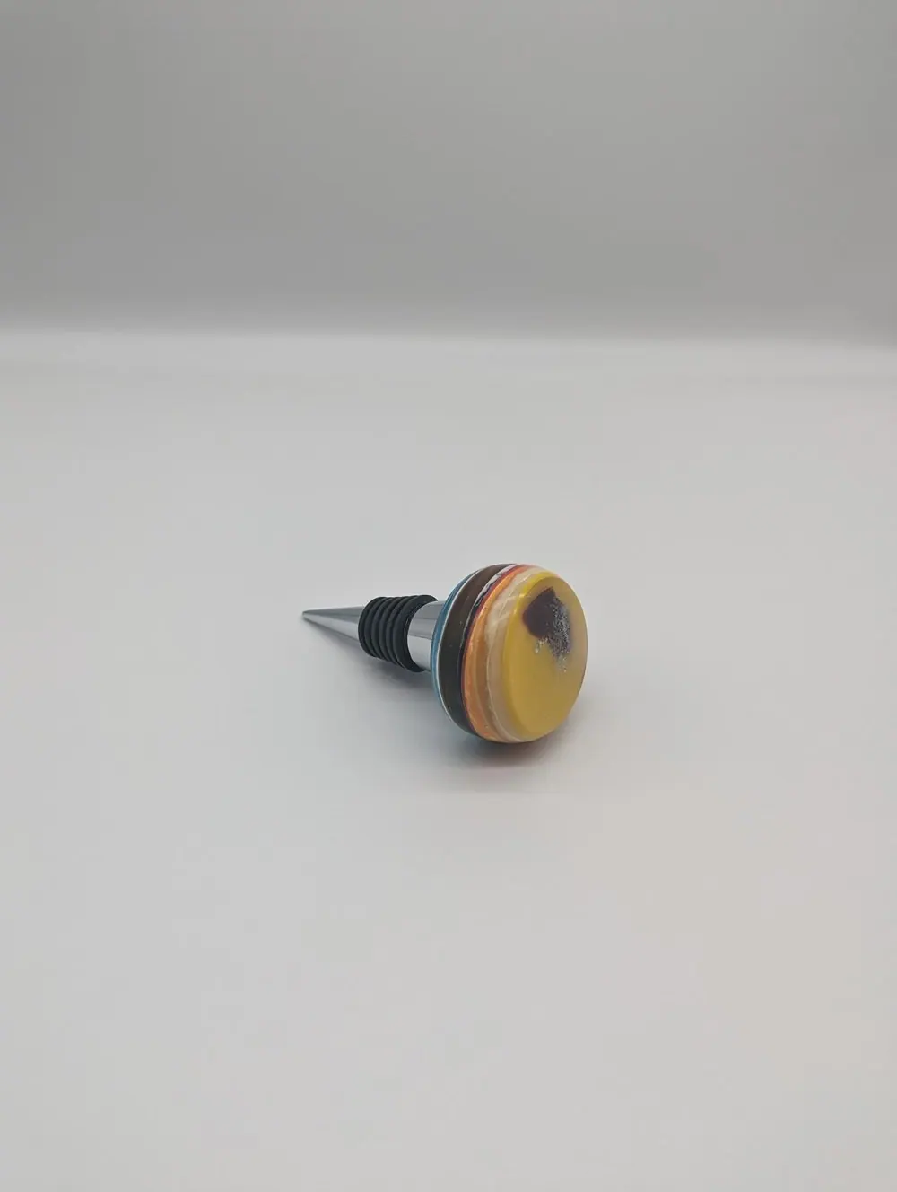 Upcycled wine stopper with layered resin top on a neutral surface.