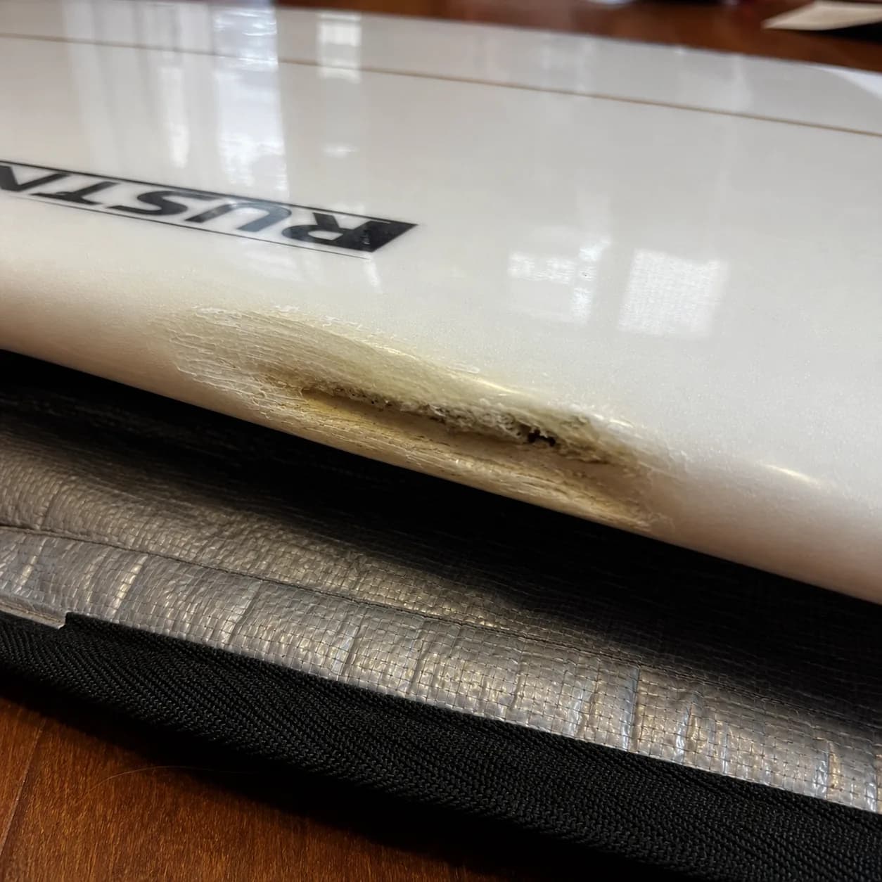 A large rail ding on a white surfboard before repair.