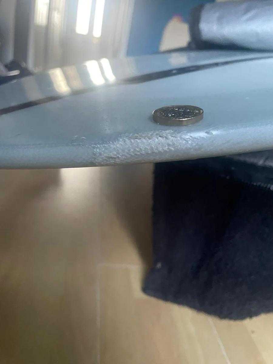 A medium rail crack on a surfboard shown beside a coin for scale.