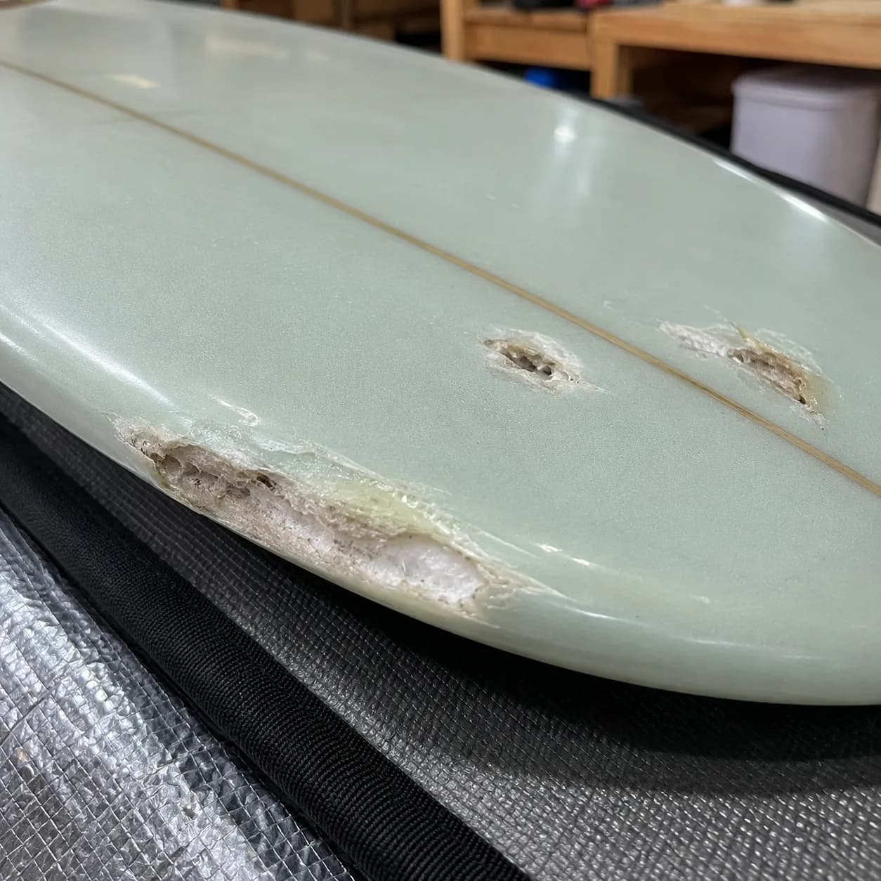 A surfboard deck showing several damaged areas and dings requiring repair.