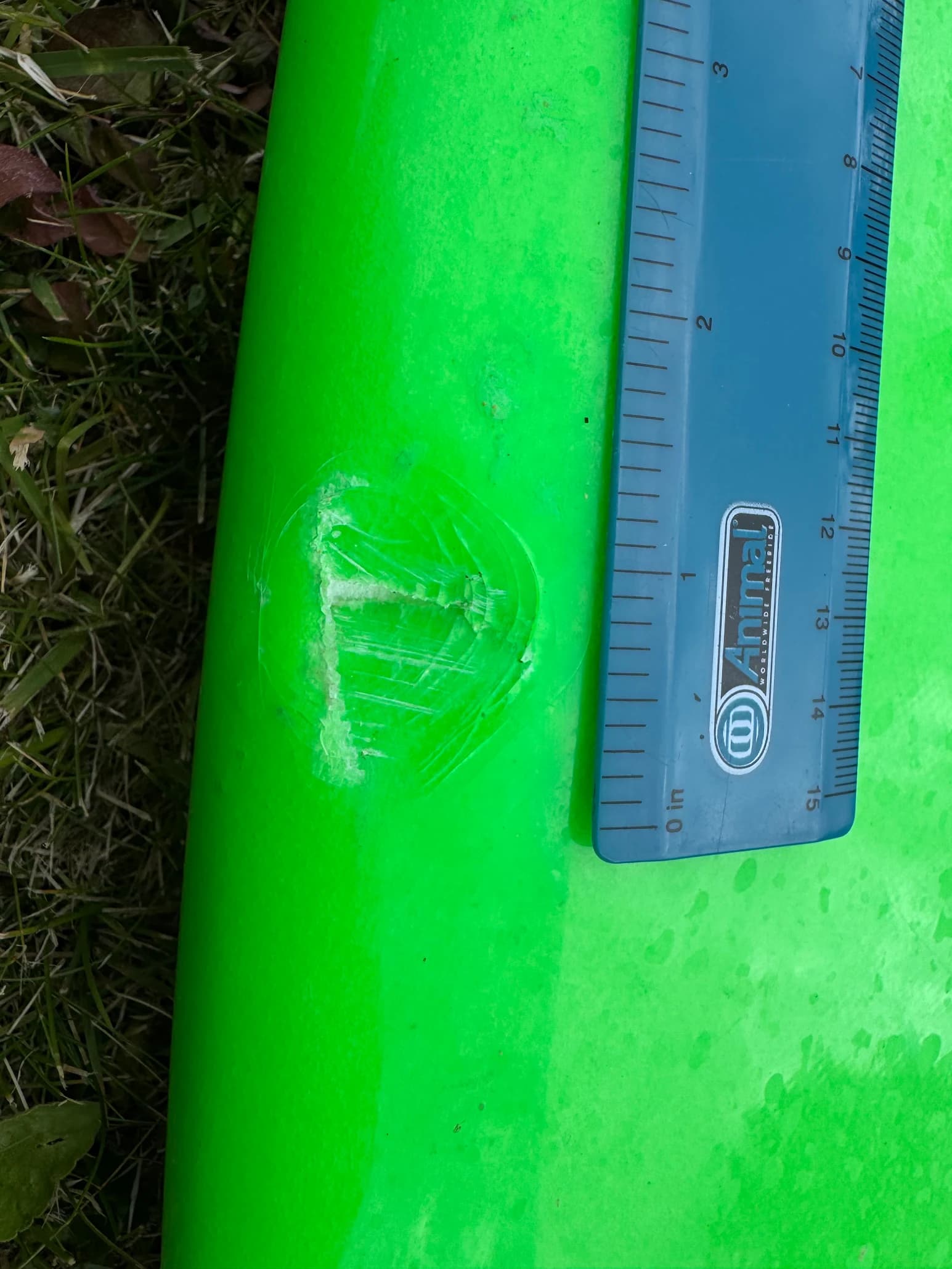 A small ding on a green surfboard shown beside a ruler.