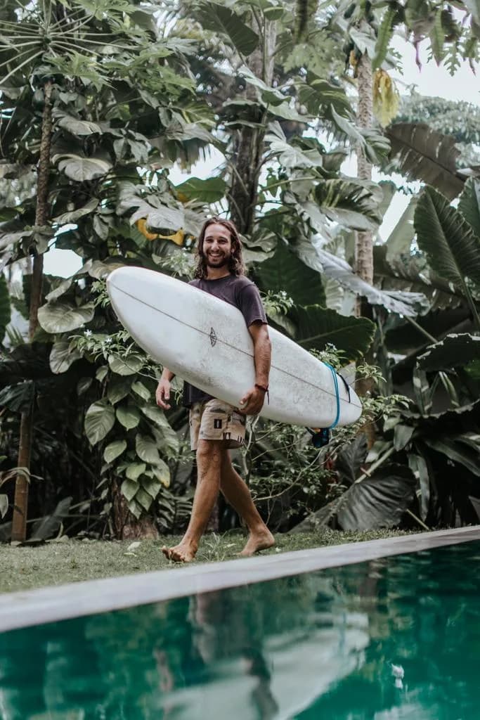 James Bailey smiling in the Whitburn Studio workshop with a surfboard.