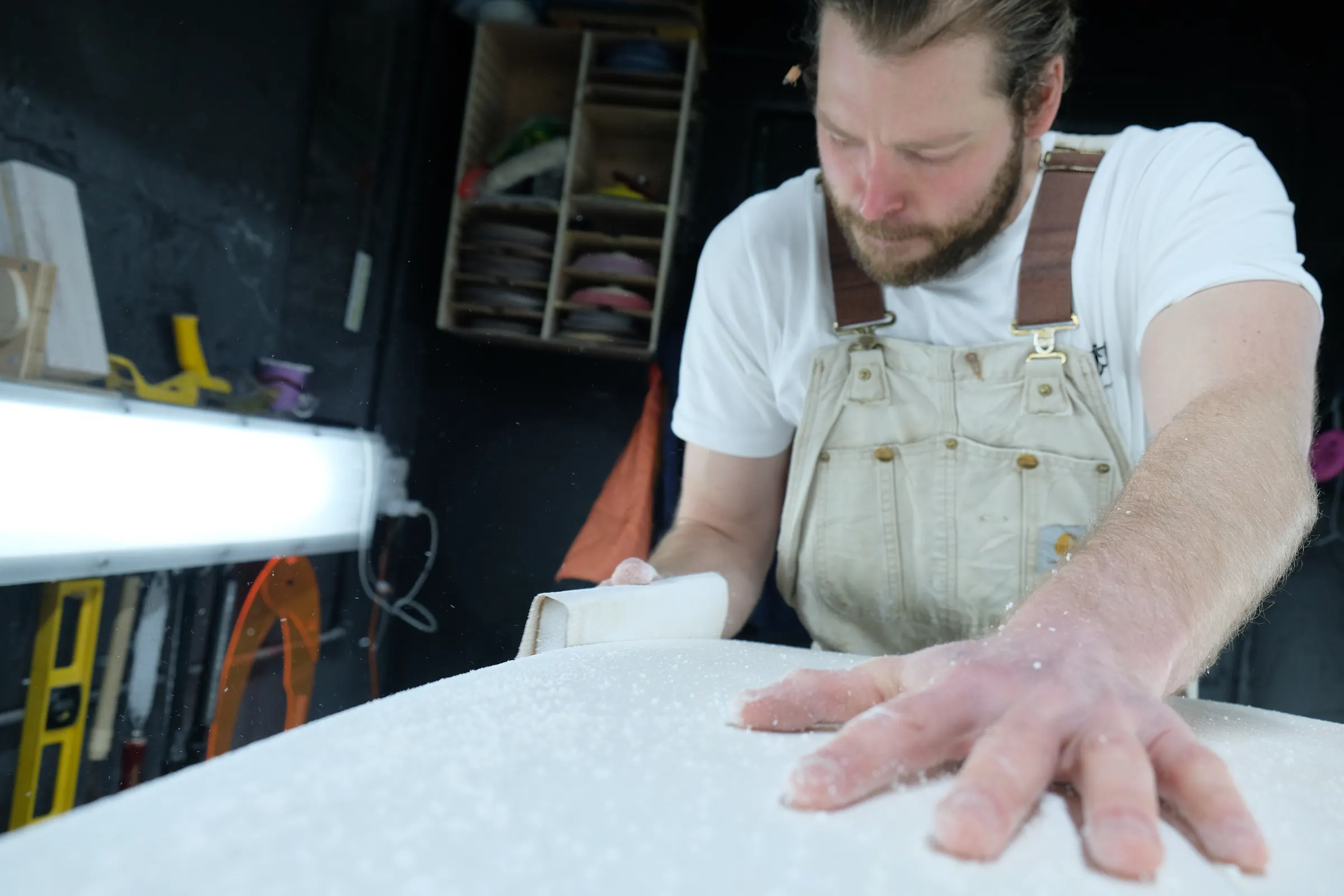James hand-sanding the rail of a surfboard blank.