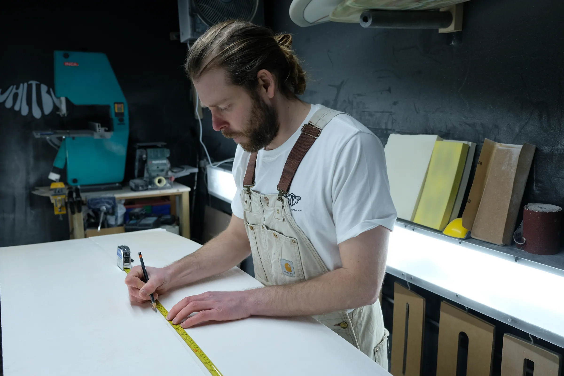 James marking measurements on a surfboard template in the workshop.