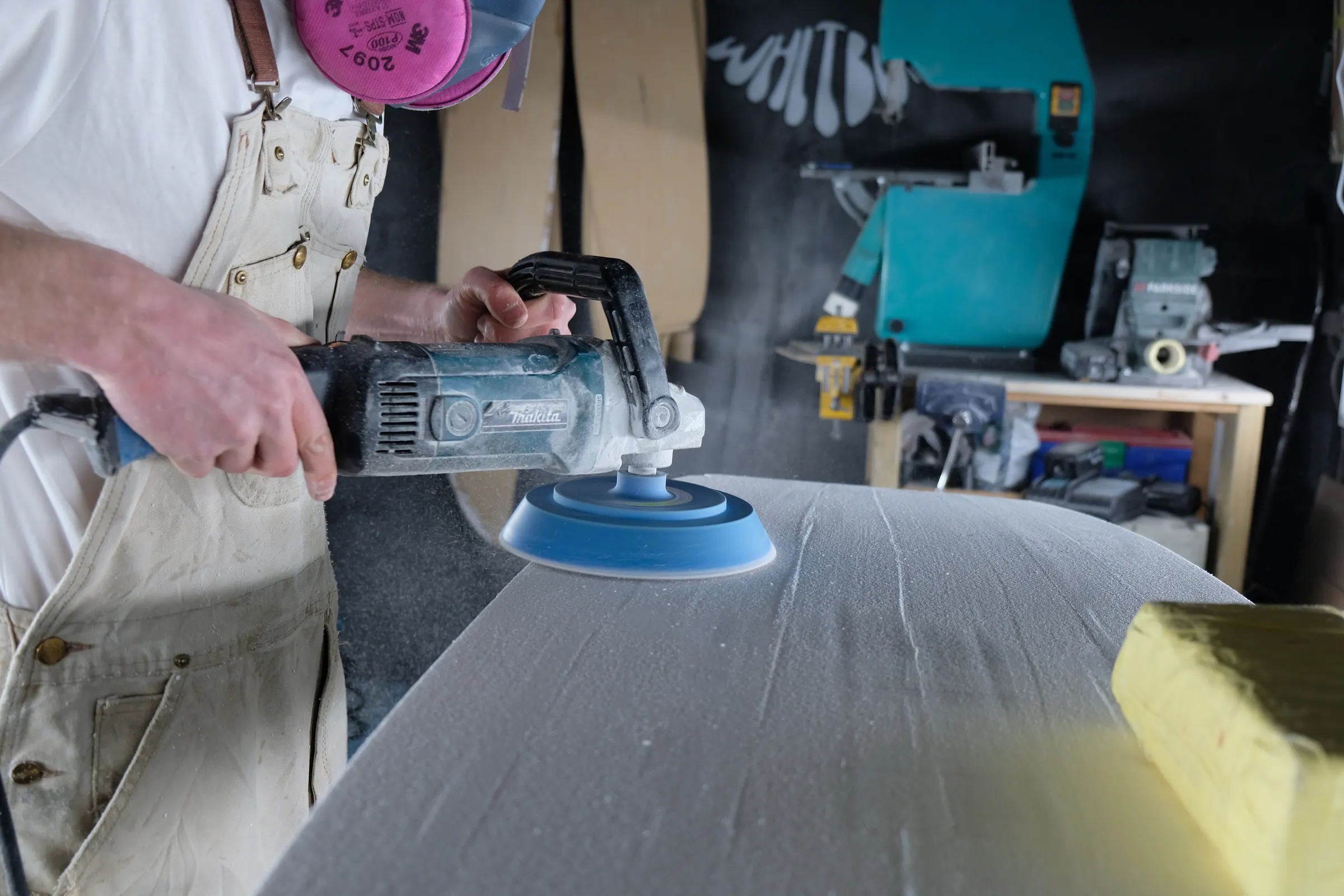 James sanding a surfboard blank with a power sander in the shaping bay.
