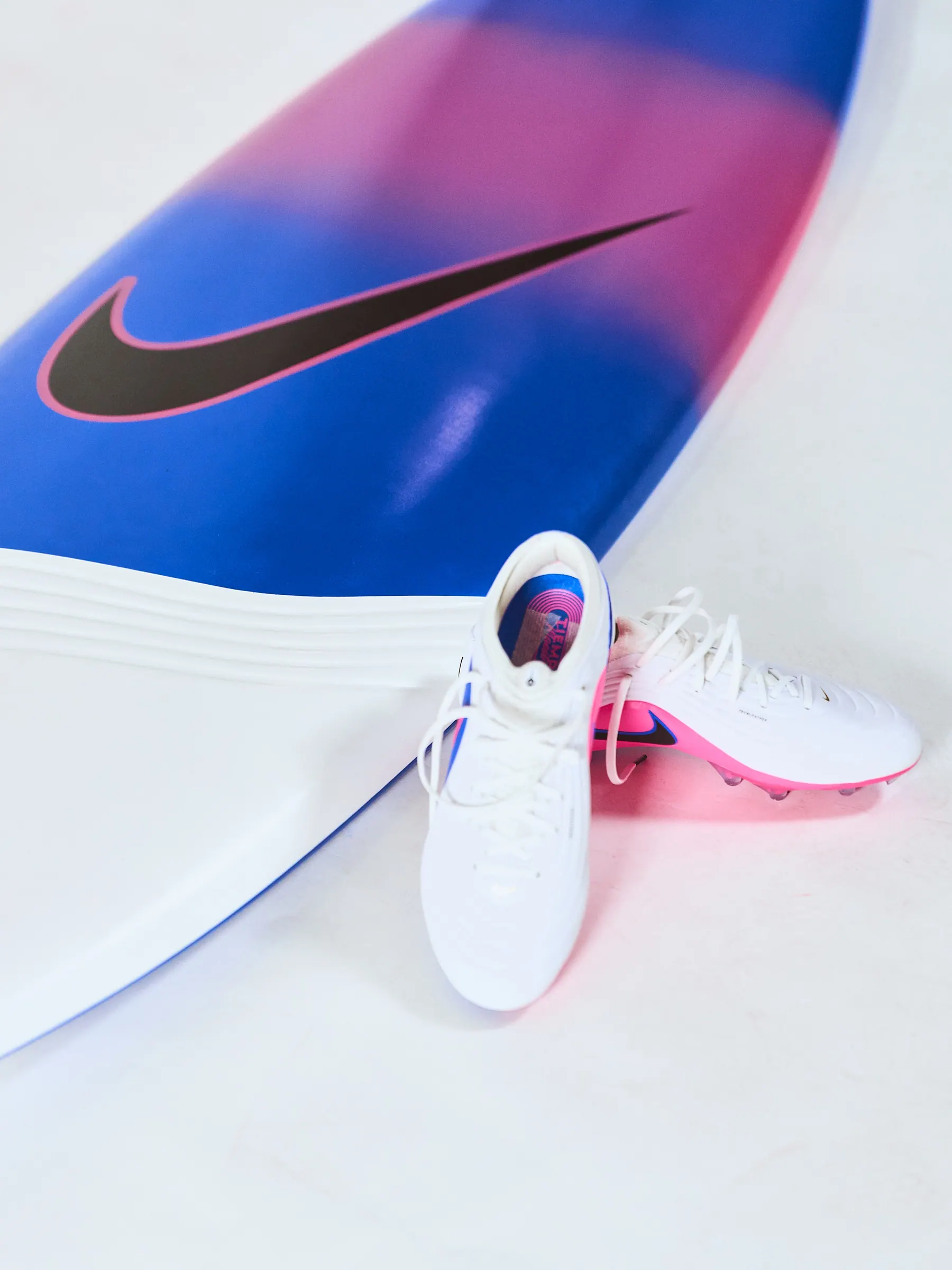 Nike Tiempo-inspired surfboard with blue and pink gradient finish beside the boot